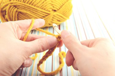 Cropped Hands Crocheting Wool Over Paper