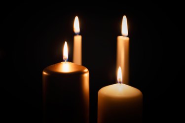 Candles burning in darkness over black background