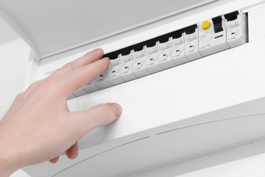 Detail of opened home white fuse box with set of black electric fuses. Male hand in position to switch a fuse off. Electricity and safety.