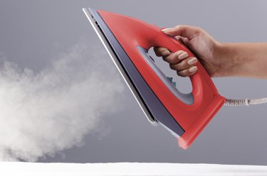 Person holding iron over gray background