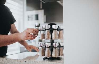 Male hand lifting one bottle from a rotating spice rack on a stone countertop