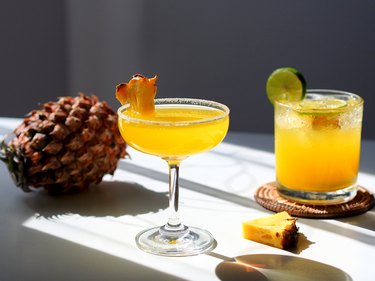 Pineapple cocktail in coupe and lowball cocktail glasses with a pineapple on the table