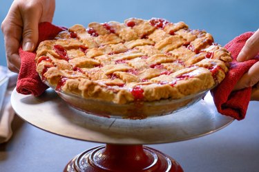 Hands putting down hot, bubbling Cherry Pie with Lattice Crust