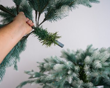 A man mounts a composite reusable spruce for the new year. Decoration for the holiday. Protection from deforestation. A man's hand holds an artificial Christmas tree