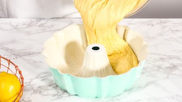 Baker pouring batter into a colorful bundt pan, on a marble countertop