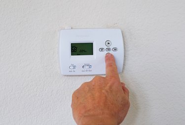 Cropped Hand Of Man Adjusting Thermostat On Wall