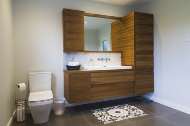 White high-back flush toilet and American walnut wood vanity with rectangular sink and ceramic tile flooring, Quebec, Canada