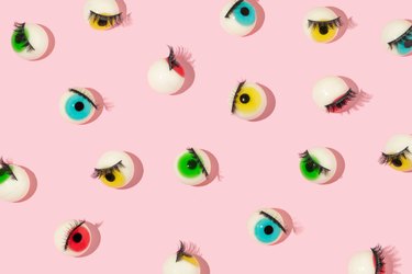 Creative pattern made with eyeball figurines with eyelashes on pastel pink background. Halloween minimal creative concept. Rainbow colored eyes. Modern fashion aesthetic or cosmetic idea.