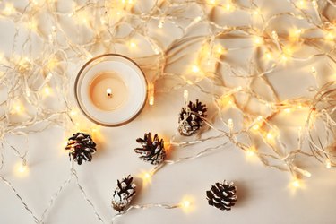 High Angle View Of Lit Candle By Illuminated Lights And Pine Cones On Table