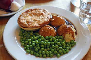 Australian traditional meat pie with meat gravy, mash potato, green peas on a white plate