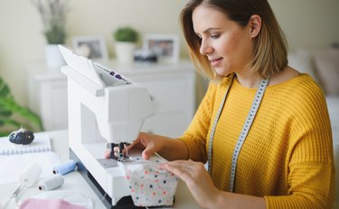 Young woman sewing protective face mask indoors at home, quarantine concept.