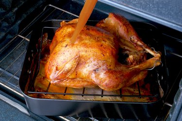 Basting a Thanksgiving turkey in a roasting pan in an oven