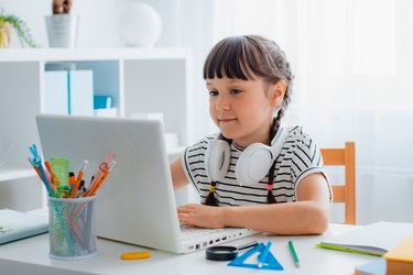 Child brunette schoolgirl studying homework during an online lesson at home in a bright white room, school time, online education concept