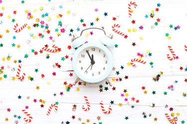 Christmas background with candy canes with alarm clock and multicolored sequins on wooden background