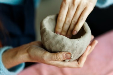 Women's hands knead the clay and sculpt a cup or bowl from it. The process of manufacturing a ceramic product,close up