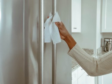 Woman Cleans Refrigerator Handle Using Disinfectant Wipe