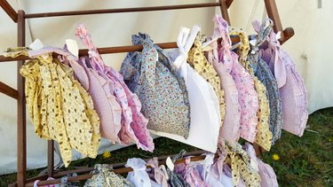 An array of cotton Civil War style ladies hats on a wooden rack against a white canvas background.