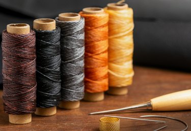 Waxed colorful sewing threads, stitching awl and needles closeup