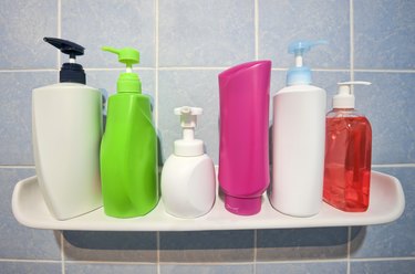 Many shampoo and soap bottles on a bathroom shelf.