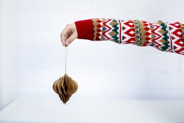 In outstretched hand in a knitted sweater holds a Christmas tree decoration made of paper diy.