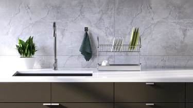 Modern and minimal built-in gray kitchen counter with white laminate top, sink and white marble tile wall in sunlight from window