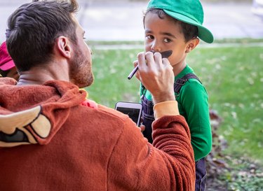 White father dressed up for Halloween painting mustaches on his African American son's face