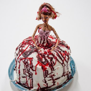 Barbie doll standing in center of blood-splattered cake.