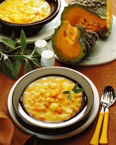 close-up of a bowl of pumpkin and macaroni kept beside pumpkin slivers and herbs
