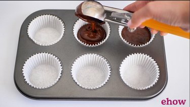 scooping cupcake batter into cupcake tray