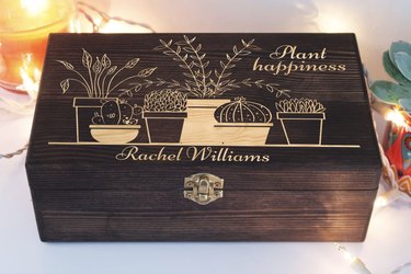 Custom seed storage box in a dark wood finish with etched images of plants. It says "Plant Happiness" and the person's name, "Rachel Williams."