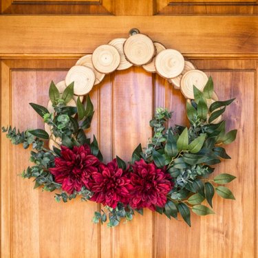 A wooden wreath with greenery and red flowers
