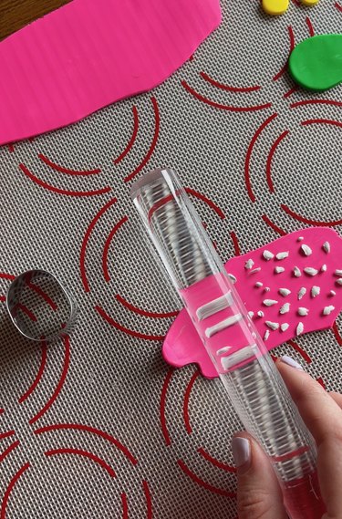 A slab of pink clay with white terrazzo flecks and an acrylic roller pushing them down.