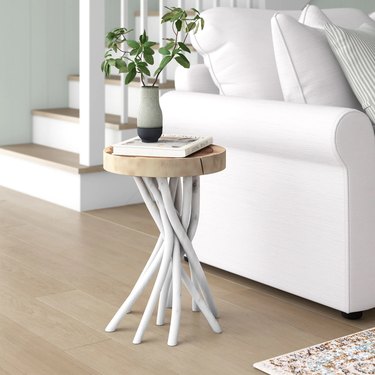 Teak wood tree stump side table with white tendril legs next to white sofa.