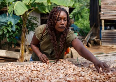 Chef Selassie Atadika reaches out to comb through cacao beans, wearing her hair in two braids and a green shirt