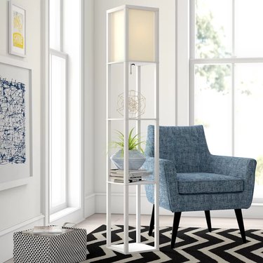 63-inch-tall column floor lamp with two shelves adjacent to blue armchair.