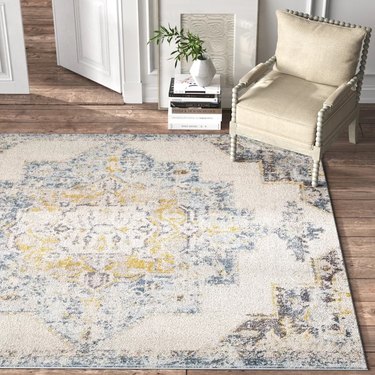 Large, Oriental-inspired area rug in muted colors on hardwood floor with sitting chair in the corner.