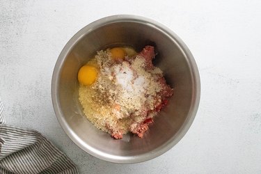 Ingredients for beef meatballs in a stainless steel bowl