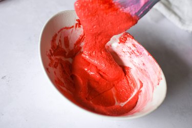 Red macaron batter flowing off a rubber spatula