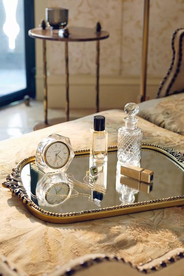 Mirrored Primrose serving tray from Anthropologie with perfume, lipstick, jewelry, and a clock sitting on it.