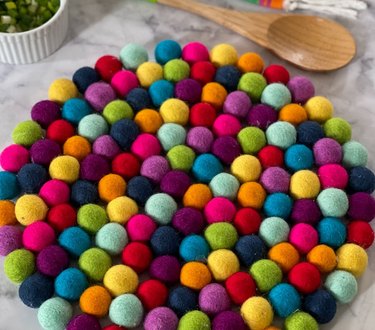 Colorful rainbow pom pom placemat on a light gray countertop with a measuring spoon nearby