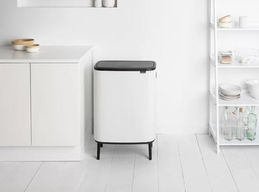 White modern trash can with a black top and black tapered legs with a touch-top.