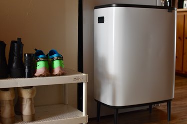 Rectangular white trash can with two compartments on black tapered legs in the entryway to a kitchen.