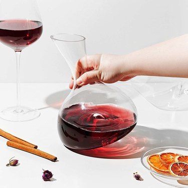 Person swirling red wine in a decanter on a white countertop.