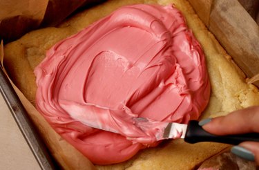 Spreading pink food coloring on sugar cookie.