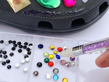 A closeup of using a wax pen to pick up rhinestones to glue