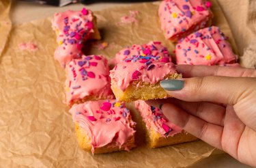 Holding a sugar cookie bars with pink frosting and sprinkles on parchment paper.