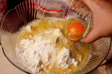 Adding an egg to a bowl with sugar cooke mix and butter.