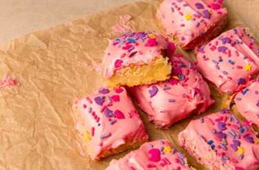 Sugar cookie bars with pink frosting and sprinkles on parchment paper.