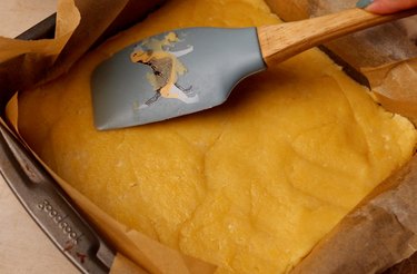 Using a silicone spatula to press cookie dough into a square pan.