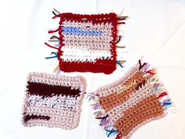 three crochet coasters in various shades of pink and red with scrap tassels